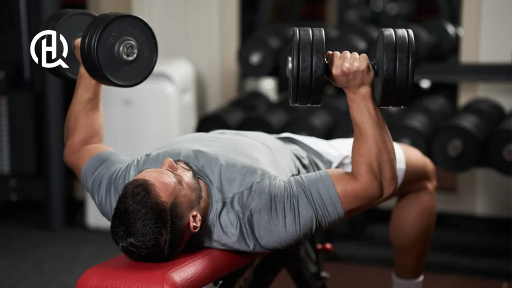 A person lying on a bench, holding dumbbells in each hand - showing how to do bench press.
