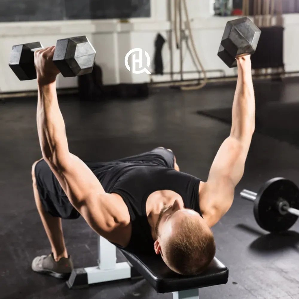 Man in a black tank top doing a flat bench dumbbell in a gym.