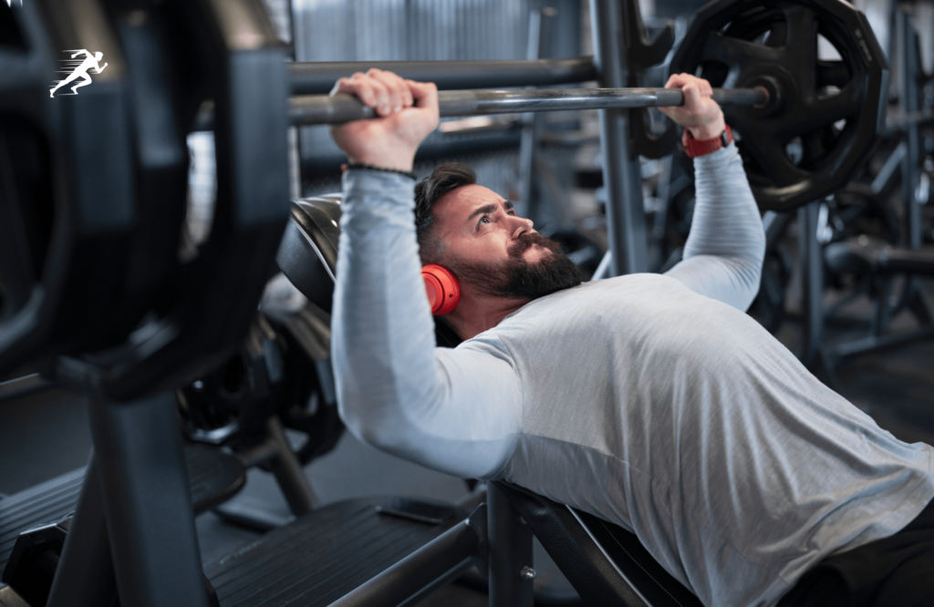 Image of a guy trying to push his PR on bench press while listening to hardcore music.