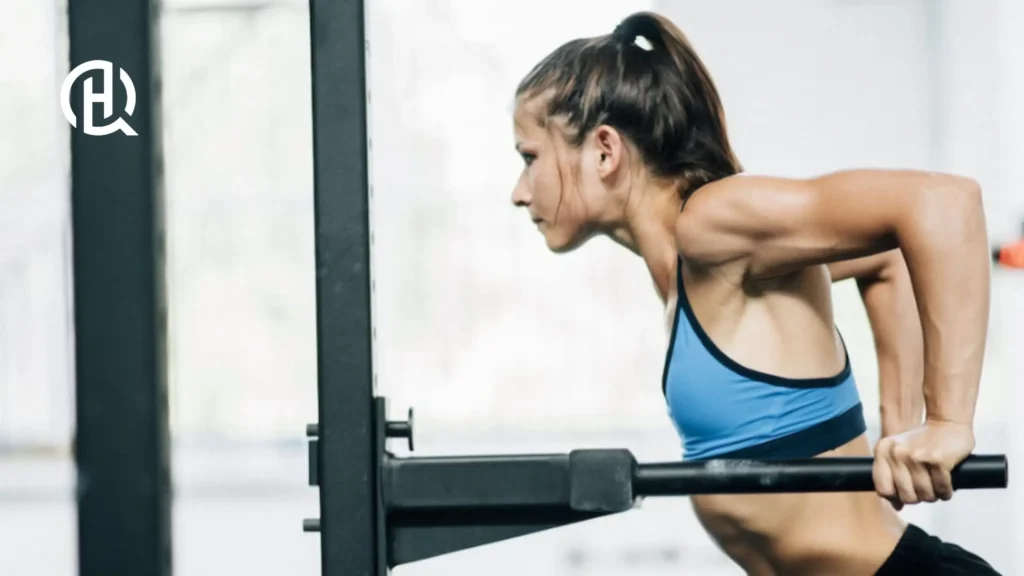 Woman doing parallel bar dips on a straight bar. She is wearing a blue top.