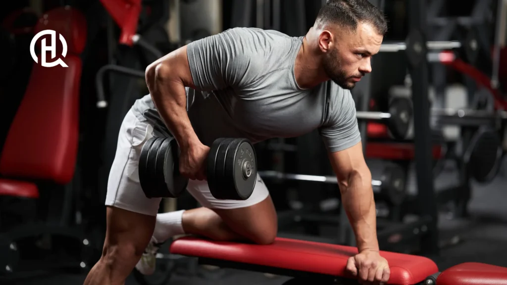 A man, looking forward as he pulls the weight up to his right side of the body. Whilst leaning on a bench.