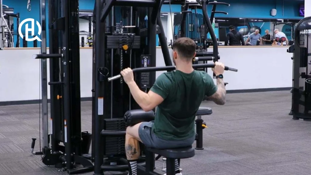 A person in a green tshirt, grey pants and some strange socks, doing lat pulldown.